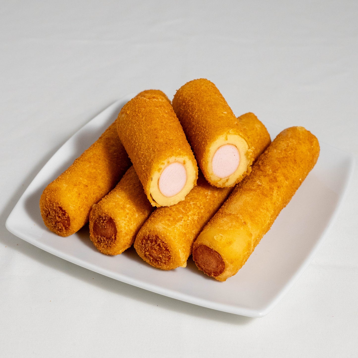 A golden-crisp breaded Brazilian sausage roll cut in half showing the savoury dough layer and the pork sausage filling inside.