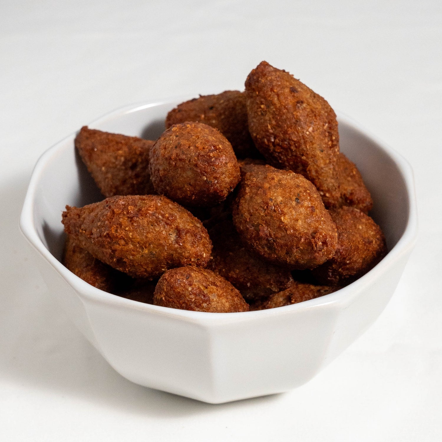A plate of 12 golden-brown crispy Brazilian kibe croquettes served hot with fresh mint leaves and lemon wedges.