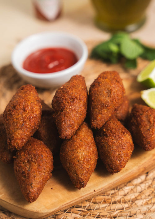 A plate of 12 golden-brown crispy Brazilian kibe croquettes served hot with fresh mint leaves and lemon wedges.