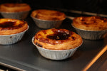 Close-up of baked Portuguese custard tarts or Pastéis de Nata served fresh from the oven with a dusting of cinnamon and powdered sugar next to an espresso coffee.