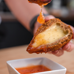A golden-brown crispy Coxibe croquette cut in half showing a spiced beef bulgur wheat shell and a melted Cheddar and Mozzarella cheese centre.