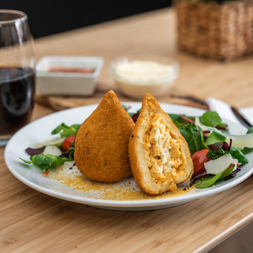 A golden-crisp big chicken coxinha cut in half revealing a generous filling of seasoned shredded chicken and melted Catupiry-style creamy cheese.